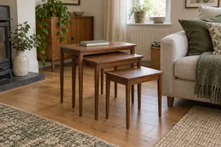 Three wooden nesting tables in graduated sizes, partly pulled out beside a linen sofa in a lived-in room.