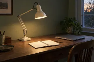 Cream articulated desk lamp with a stepped base directing light onto an open notebook on a wooden desk