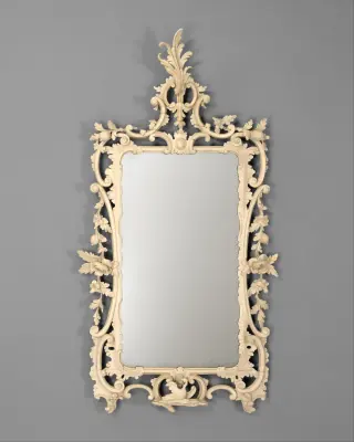 A tall eighteenth-century looking glass with a pale carved floral frame around a narrower rectangular reflective opening.