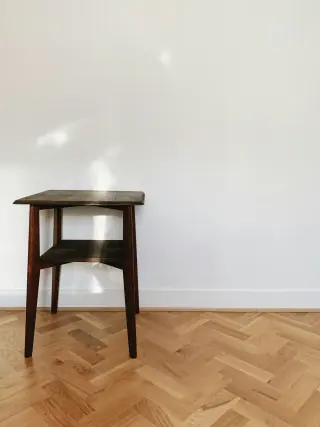 Small wooden stool with splayed legs standing on a herringbone wooden floor.