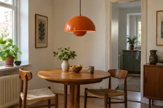An orange pendant with two hemispherical shades hanging over a wooden dining table.