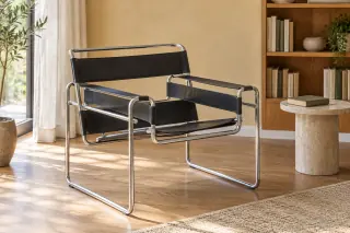 A black sling chair with an open tubular metal frame stands beside a small reading table and wooden bookcase.