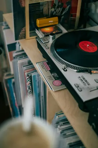 Record player on a wooden shelf with sleeved records stored beneath and behind it.