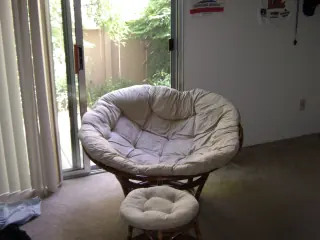 A round cushioned Papasan chair paired with a smaller round cushioned footstool in front of it.