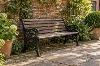 A wooden-slat bench with dark cast-metal end frames stands in a planted brick courtyard.