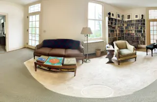 A sofa with three separate seat cushions in the Carl Sandburg Home living room, seen from the front with its wooden base and feet visible.