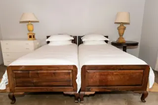 Two wooden bed frames placed side by side with separate mattresses, lamps and differently shaped bedside furniture.