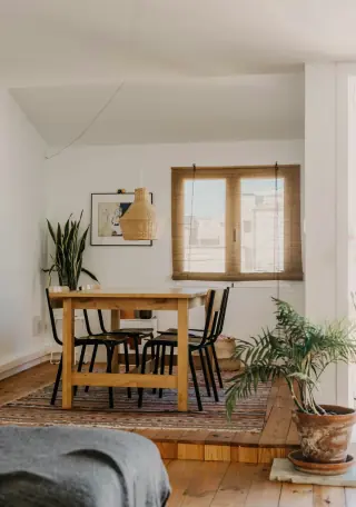 Wooden dining table with several slim-backed chairs beside a window, a rug and nearby furniture.