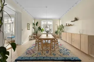 Long dining table and wooden chairs on a patterned rug, with a sideboard and a walking route alongside.
