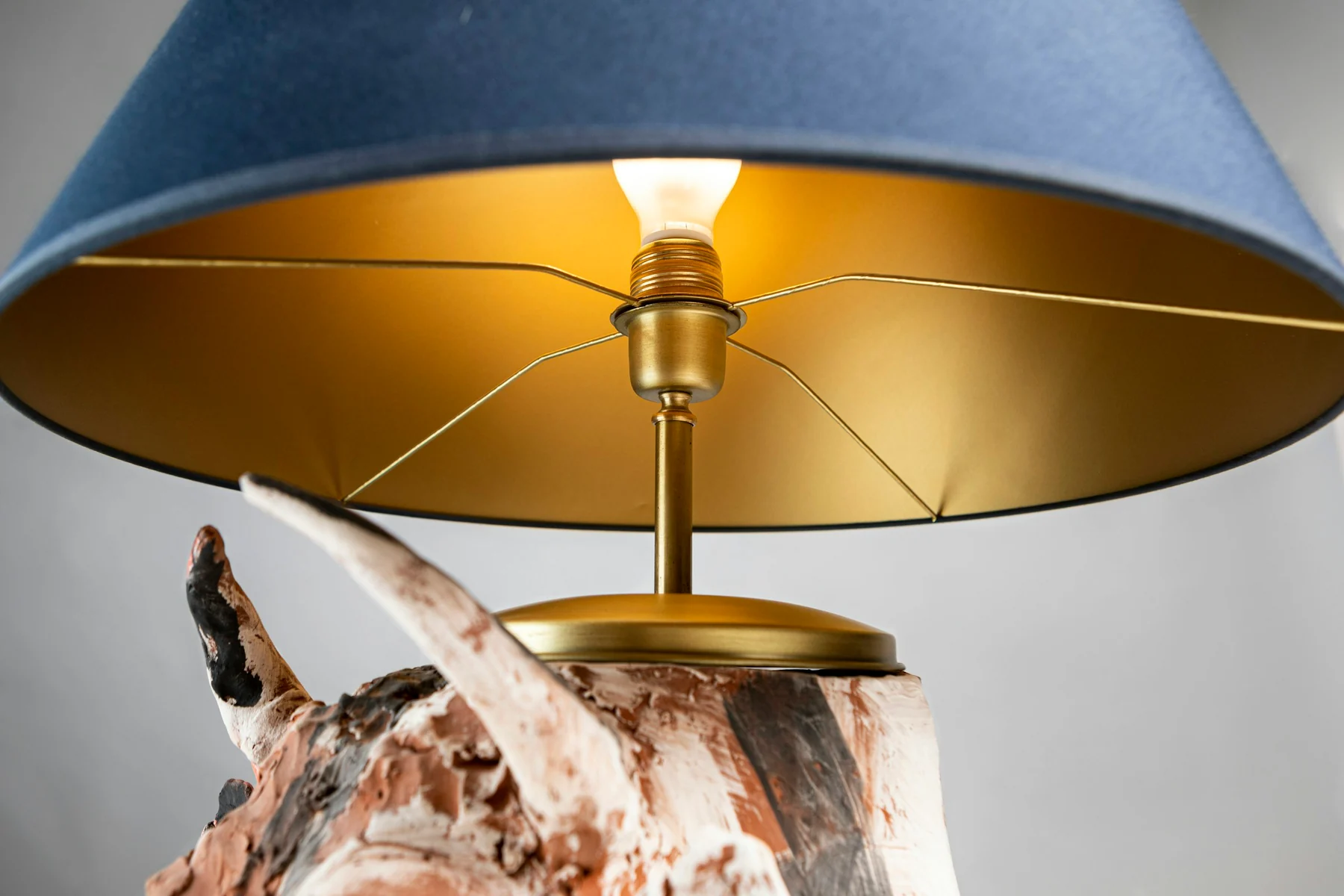 Low view into a blue lampshade showing its gold-coloured lining, support spokes and visible bulb above a decorative base.