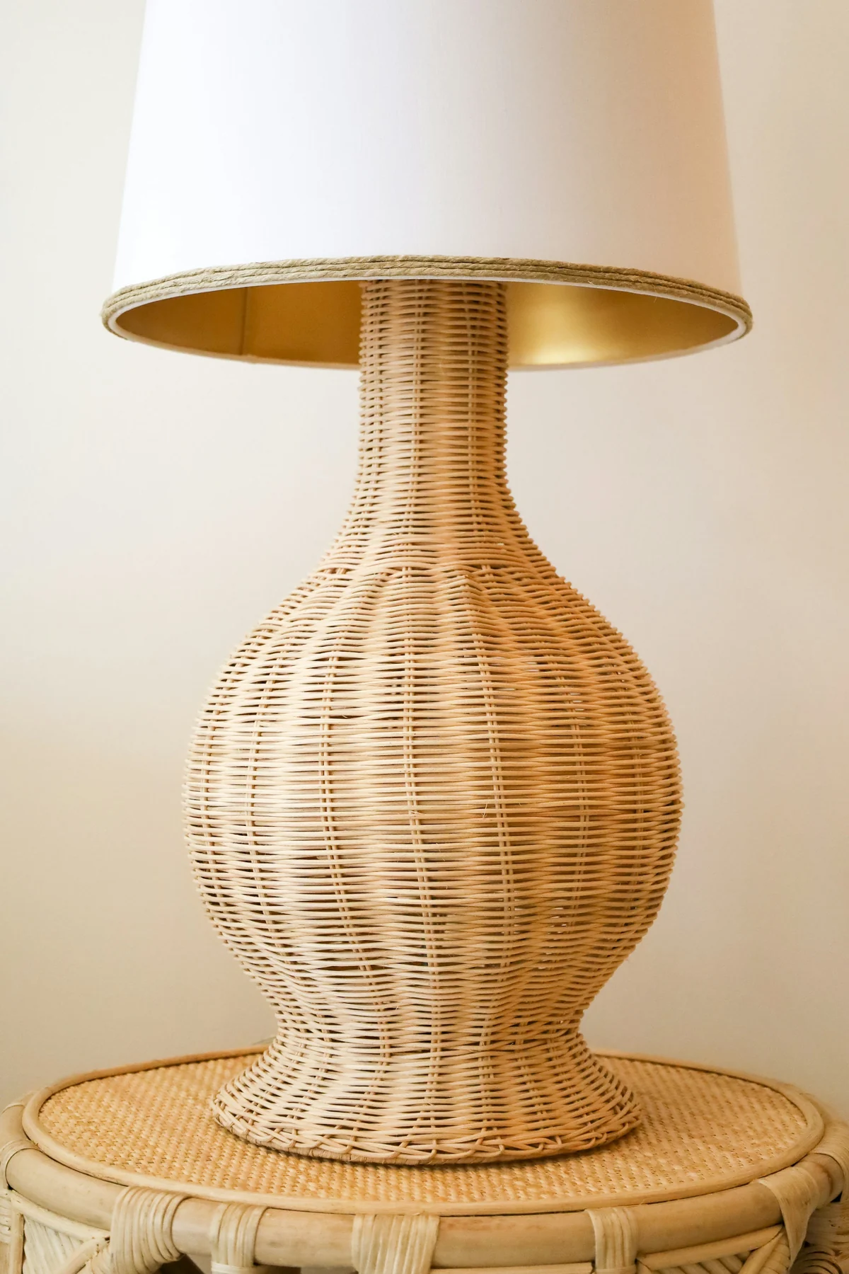 Rounded woven lamp base with a pale tapered shade on a circular woven side table.
