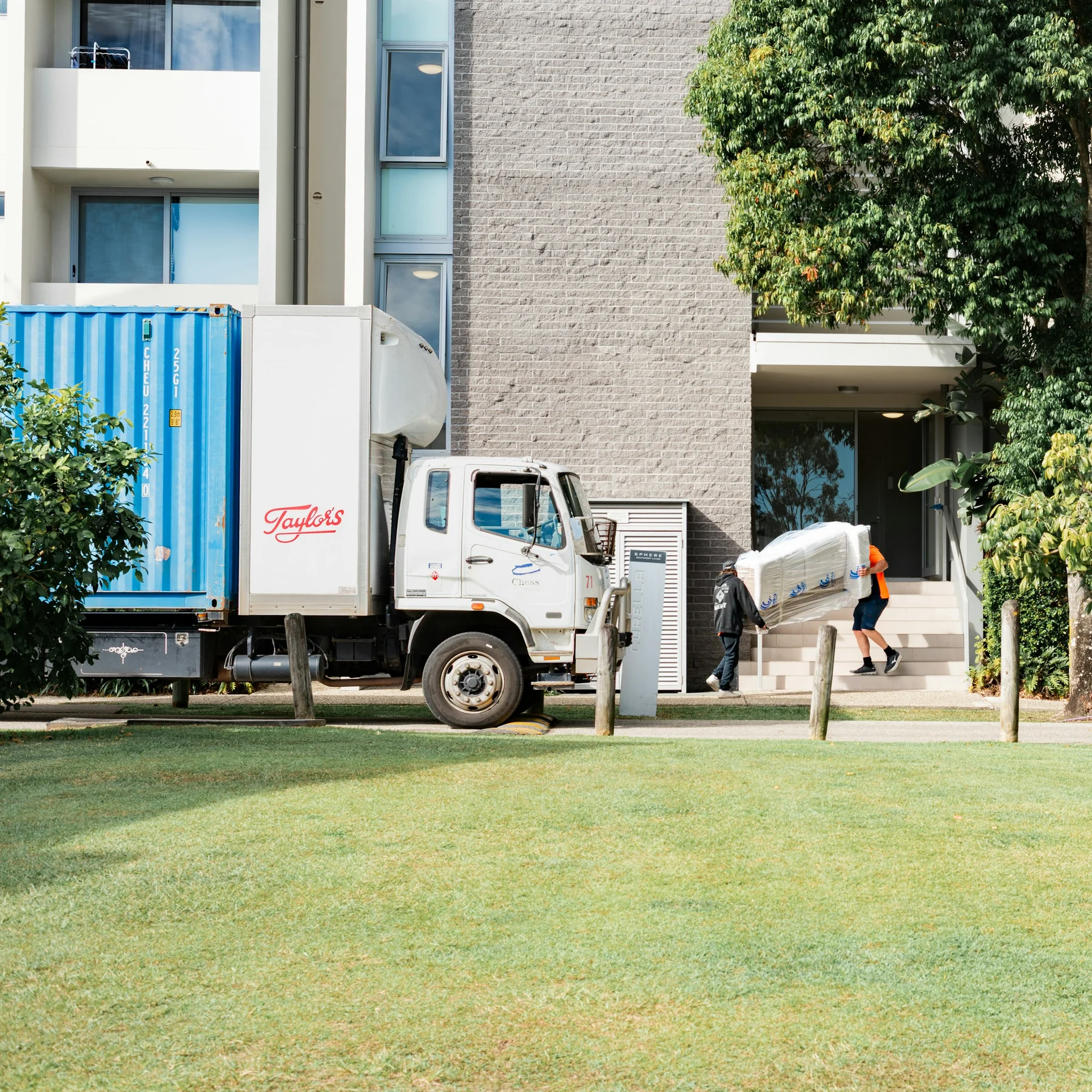 Furniture delivery truck parked beside an apartment building, with a wrapped item being carried along the approach.