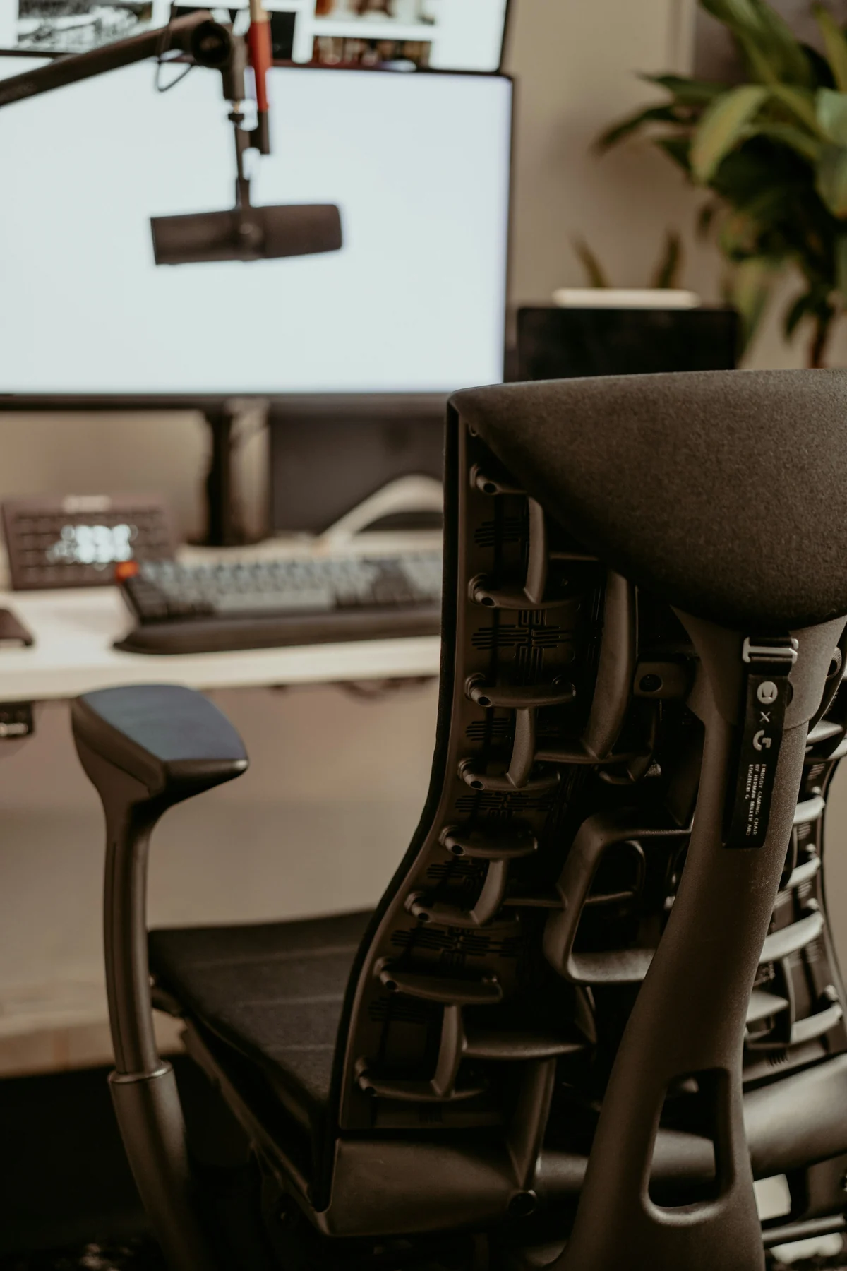 Rear view of a dark office chair showing its open back support, armrest and desk beyond.