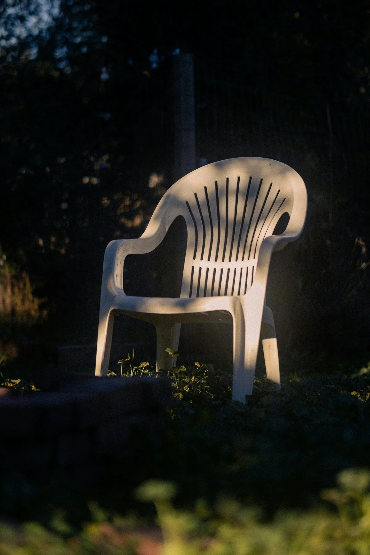 Light-coloured moulded garden armchair on grass with its back and arms in sunlight and its lower frame in shade.