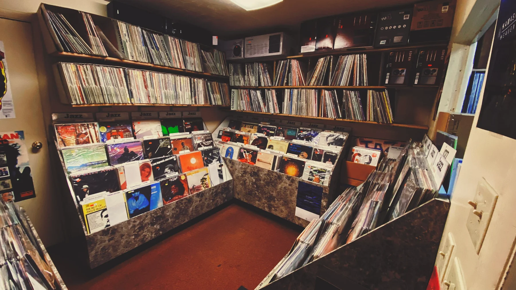 Record shop with sleeved albums in shelf rows and front-facing browsing bins around an aisle.