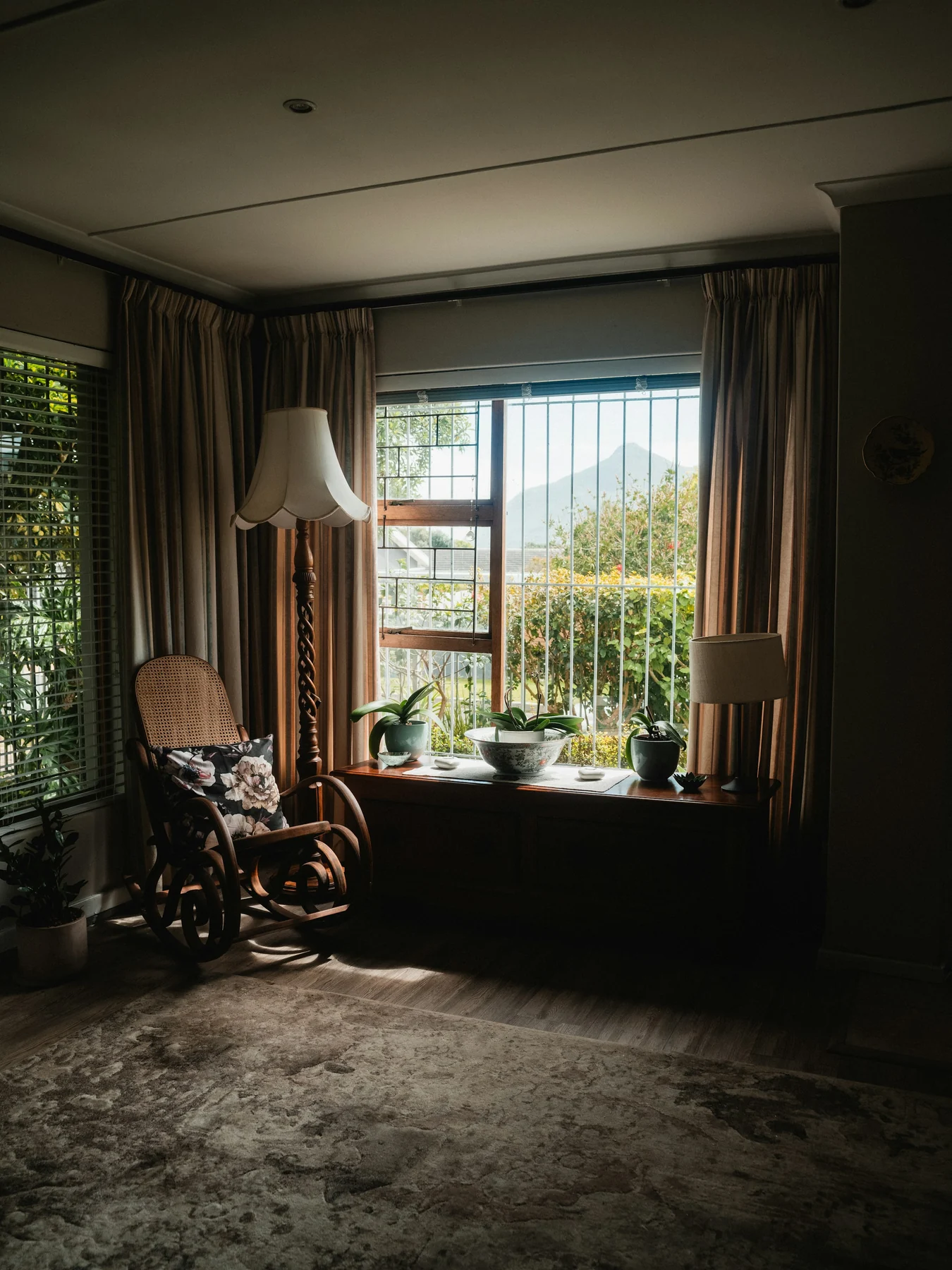 Wooden rocking chair beside a large window, floor lamp and curtains in a furnished living room.