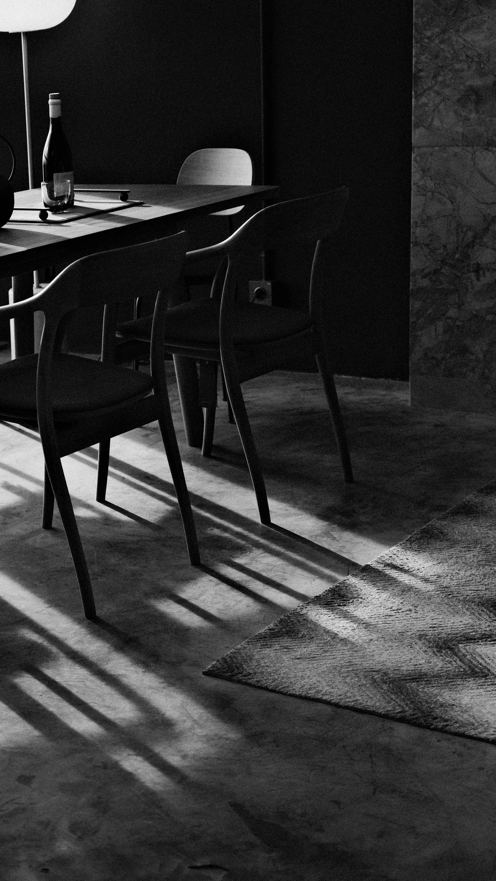 Dark dining chairs beside a table, casting long shadows across a textured rug.