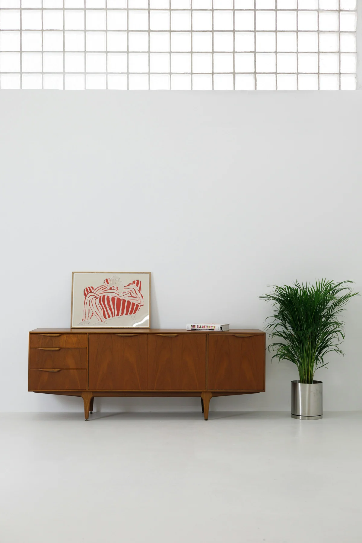Long wooden sideboard with door and drawer fronts on tapered legs against a pale wall.