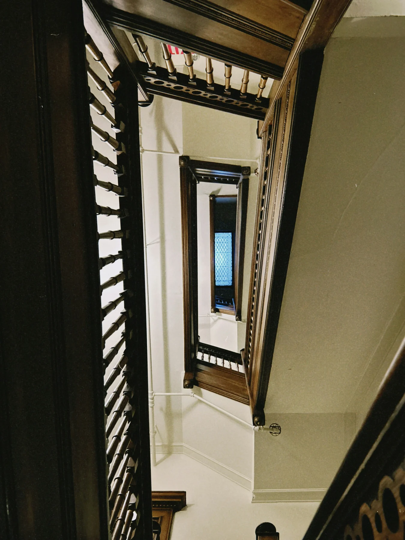 View down an old stairwell showing successive wooden landings, turns, handrails and the opening between flights.