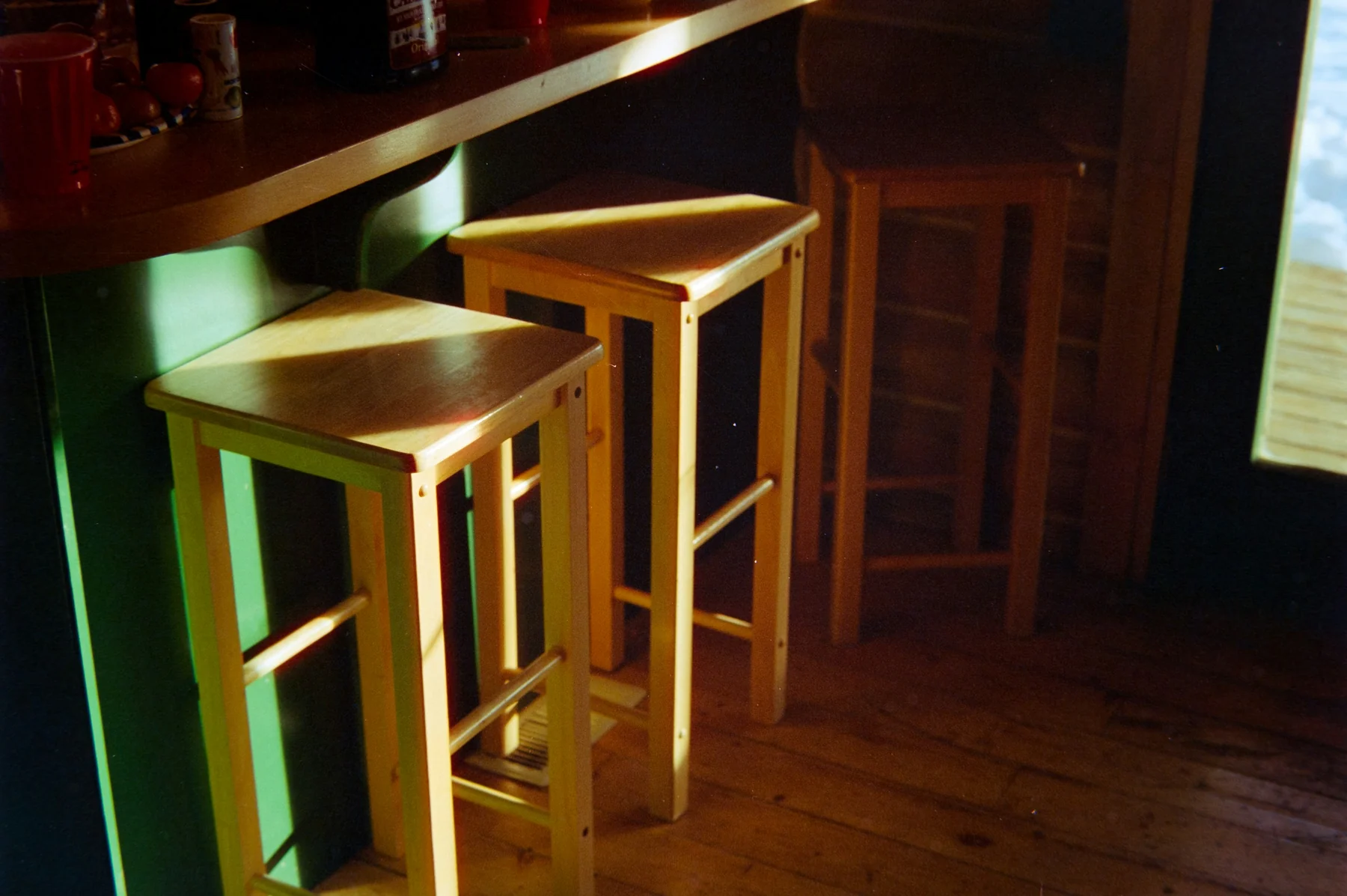 Two square wooden backless stools at a counter, with their foot rails and the counter underside visible.