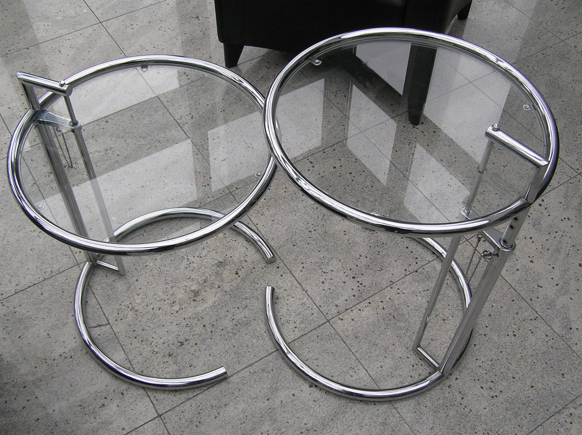Overhead view of two circular glass-top E-1027 tables showing transparent panes, small contact points, offset steel uprights and open ring bases.