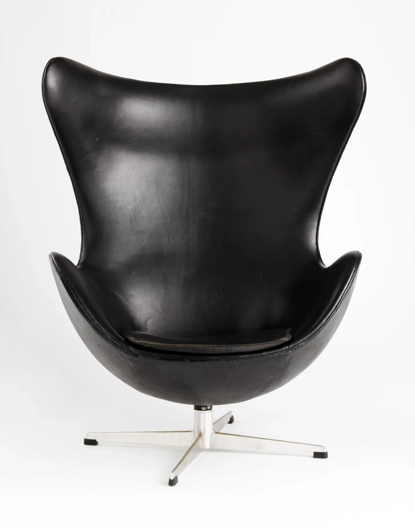 Front view of a black leather Egg Chair with a broad curved back, raised wings, seat cushion, stitched edges and aluminium star base.