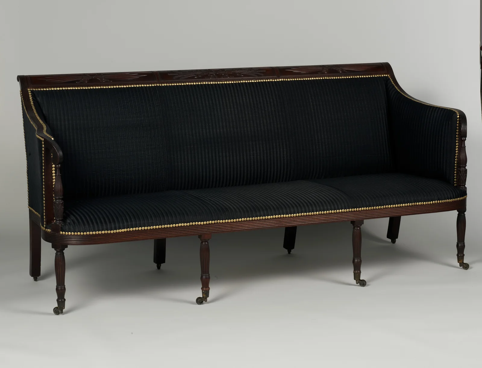 A dark upholstered early nineteenth-century sofa is shown in full from the front and side, including its curved arms, wooden frame, multiple legs and castors.