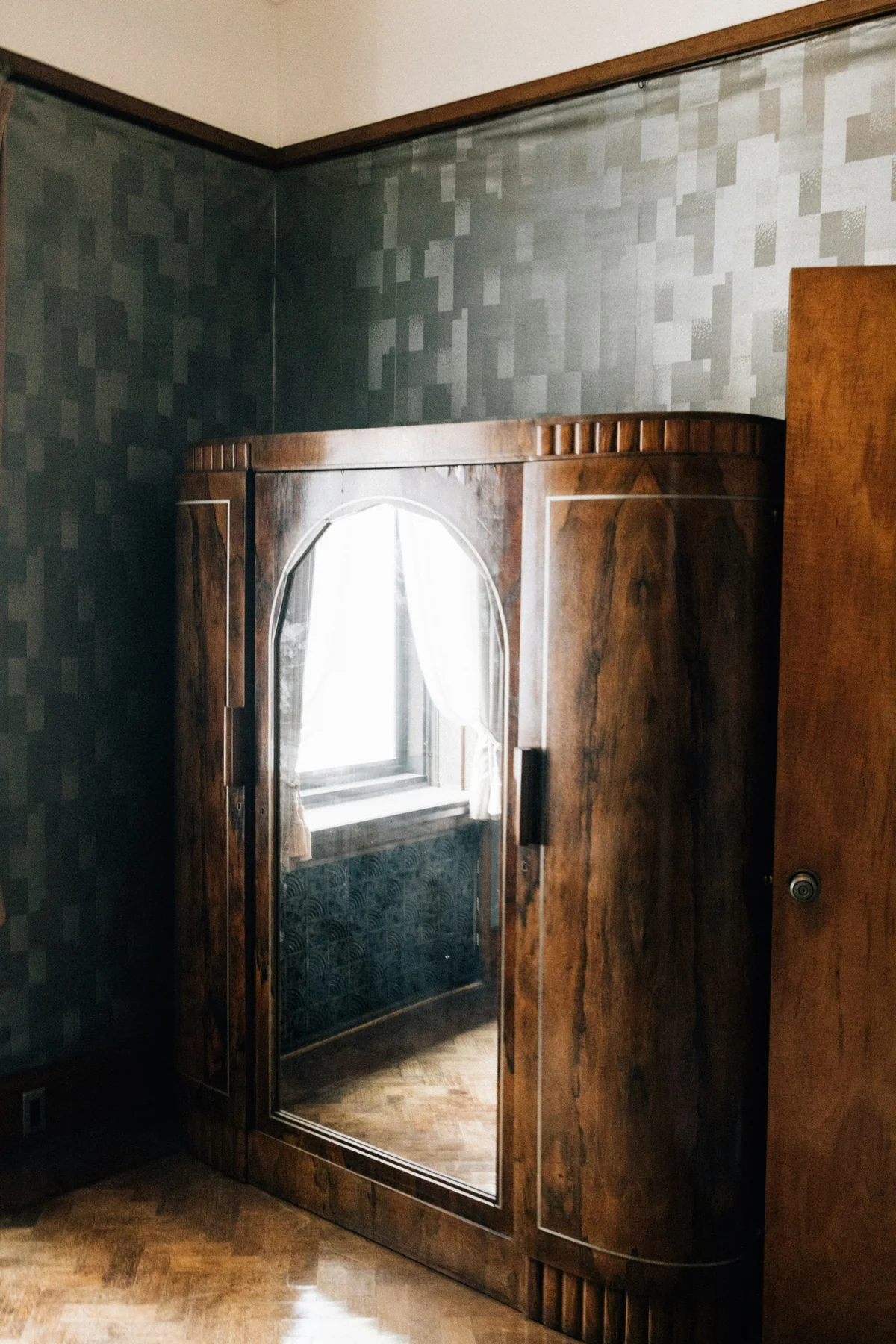Tall wooden wardrobe with a mirrored central door, rounded corners and a projecting base in a bedroom.