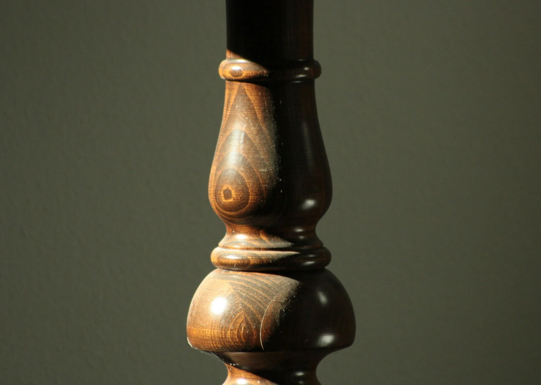 Close view of a dark turned wooden furniture leg with a pale worn patch and changing surface sheen.